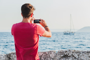 Young man tourist taking photo with smartphone by the sea