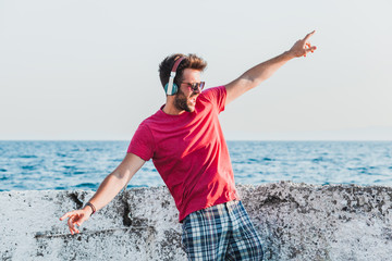 Young man listening to the music on headphones by the sea