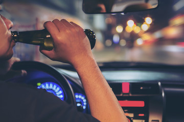 Man drink beer while driving at night in the city dangerously, left hand drive system