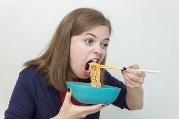 Young caucasian girl eating noodles using chopsticks