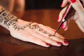Master mehndi draws henna on a female hand.