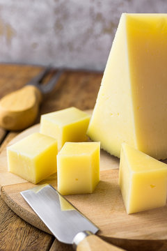 Wedge Of Spanish Cured Hard Goat Cow And Ewe Cheese Cut In Cubes On Wood Platter. Knife And Fork On Table. Traditional Appetizer, Tapas, Mediterranean Cuisine.