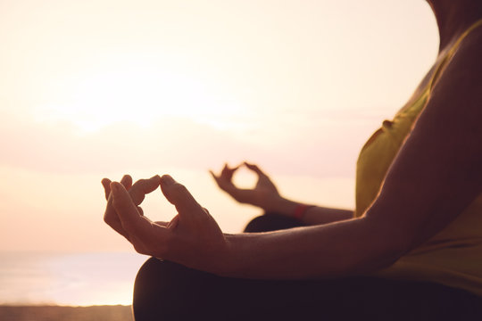 Hands of mature woman practicing yoga at lotus pose, at the sea beach