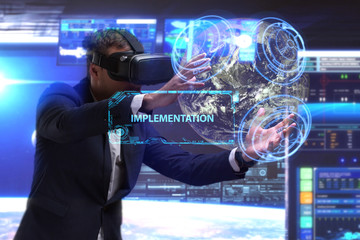 Fototapeta na wymiar Business, Technology, Internet and network concept. Young businessman working in virtual reality glasses sees the inscription: Implementation