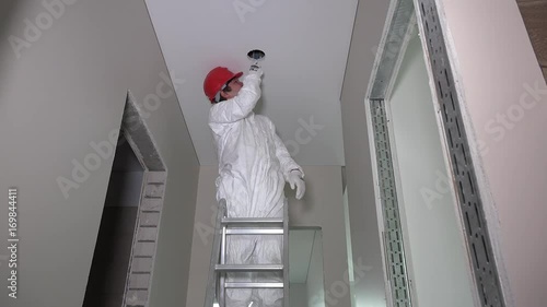 Male Worker Standing On Ladder And Cutting Hole In Corridor
