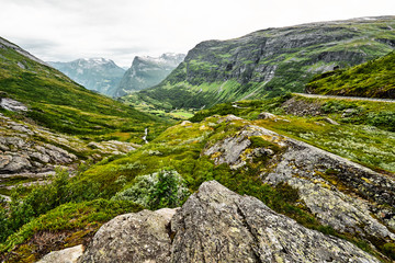 Fototapeta na wymiar Path over green pasture in the mountains of Western Norway with snow on the summits and a dark cloudy sky