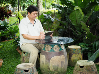 A man and his tablet sit in the garden.