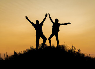 Fototapeta na wymiar Two people between clouds Full length silhouette of happy couple stand together on peak of a mountain with hands raised up, sunset and ocean. Man and woman on top mountain look at beautiful night