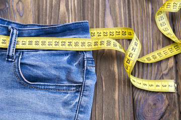 Healthy lifestyle and nutrition concept. Blue jeans with a measuring tape instead of a belt. Close up of jeans with a measuring tape around the waist. 