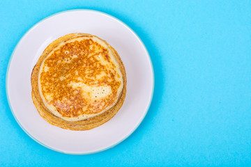 Stack of fresh delicious pancakes on white plate on blue backgro