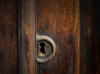 Detail of a dusty old keyhole in the door of a antique cabinet. The wood has warm tones and the keyhole is covered in dust and dirt