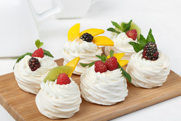 Homemade mini pavlova cakes with whipped cream and fresh berries on light  background.