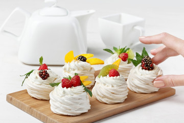 Homemade mini pavlova cakes with whipped cream and fresh berries on light  background. Selective...