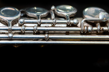 symphonic music concept - closeup on western concert flute body lies on the pure black surface, middle section with keys of the instrument, studing and orchestra concerts usage, macro