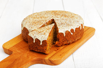 Homemade sweet carrot cake with walnuts, cinnamon and white icing on white wooden table