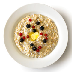 White bowl of oats porridge with chia seeds, berries and butter isolated on white from above.
