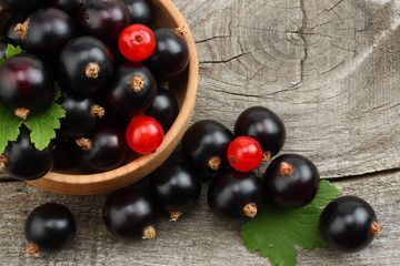 black currant in wooden bowl with green leaf on old wooden background. top view