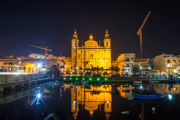 Fototapeta na wymiar The beautiful Msida Parish Church at deep night with harbor at the foreground. Malta.