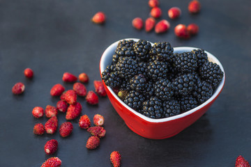 juicy blackberris in bowl shape heart on black stone background