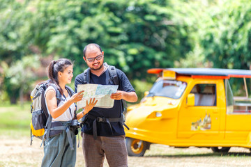 Asians love couple enjoying look at map travel with yellow taxi or tuk tuk touring background,...