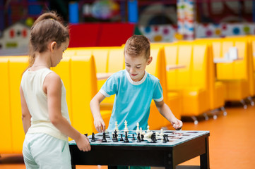 A boy and a girl are playing at a chess table