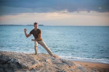 Fototapeta na wymiar gray-haired man practicing tai-chi on the beach at sunrise