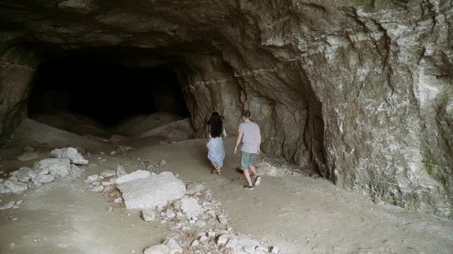 A guy and a girl are running into a huge cave. The girl runs away from the guy into the cave.