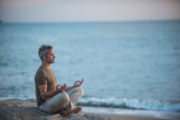  gray-haired man practicing yoga on the beach at sunrise - Powered by Adobe