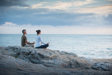 Couple practicing yoga at sunrise on the beach facing the sea