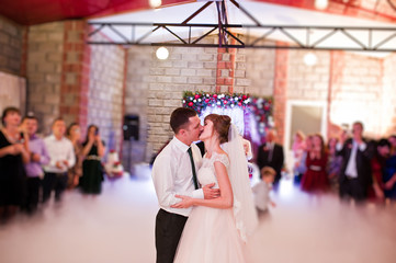 Wedding couple dancing their first wedding dance with heavy smoke and different lights in the restaurant full of guests.