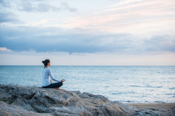 Beautiful woman practicing yoga on the beach at sunrise