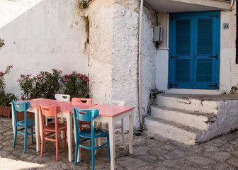 Fototapeta na wymiar Old streets and houses of Marmaris. Table with colorful chairs (blue, pink, white) stands near entrance to the house with blue east Oriental input doors in old town of the resort of Marmaris in Turkey