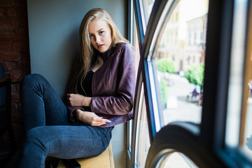 Young woman is sitting on a window sill in a cafe and enjoy free time