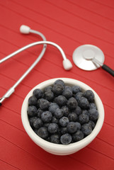 blueberries and stethoscope in white bowl over red background