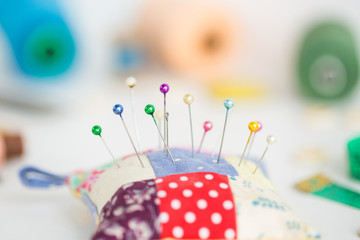 needlework, craft, sewing and tailoring concept - macro with colorful stitched pincushion and beautiful pins, measuring meter, pink, blue and green thread spools, white buttons, soap, selective focus