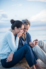 A couple sitting at the beach, looking at photos on a phone