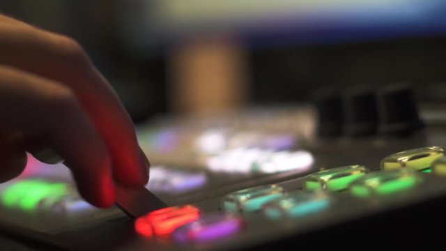 Hand moves a fader bar up to make a transition on a video switcher control panel. The lights on the panel buttons swap colors to reflect the change.
