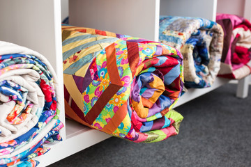 patchwork, sewing and fashion concept - some colorful finished quilted blanket in the studio at white shelves with few storage compartments, the warehouse of finished products, side view