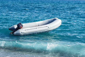 Naklejka premium Inflatable boat with a motor swings on sea waves near the shore