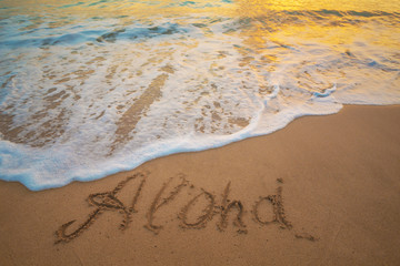 Aloha written on hawaiian beach sand with sea foam