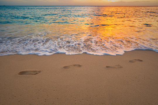 Footprints on beach sand with sea wave with foam at sunset time. Foot steps among waterline tropical vacation design