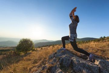 Young woman exercising on mountain on idyllic field at sunset