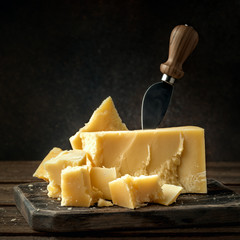 Parmesan cheese on a wooden board with knife. Pieces of parmigiano reggiano cheese.