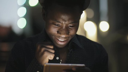 Young african man looking broadcasting online football match on smartphone in city at night