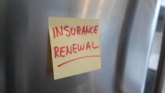 Putting an Insurance sticky note reminder on a fridge. Closeup on the hand and paper.