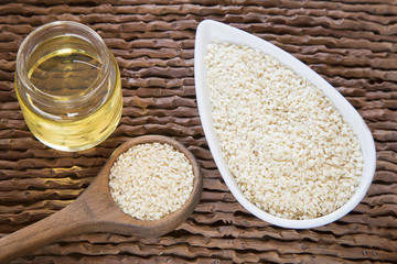 Sesame oil in glass jar and sesame seeds on wooden spoon - Sesamum indicum