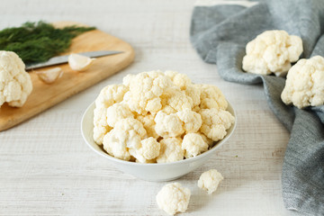 Fresh cauliflower cut into small pieces in ceramic bowl on wooden background