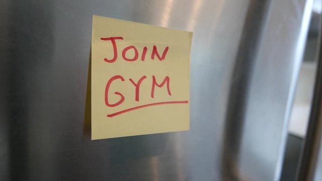 Putting a join Gym sticky note reminder on a fridge. Closeup on the hand and paper.
