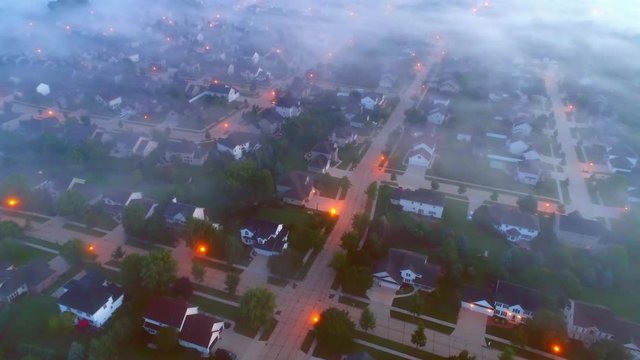 Tranquil urban neighborhoods still asleep under foggy twilight, aerial view.
