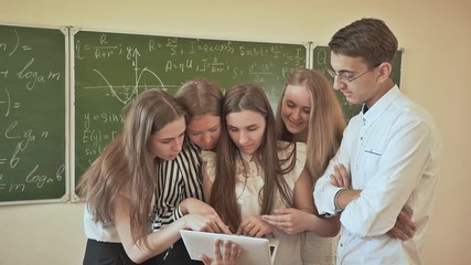 Students in the class discuss something on the laptop. Against the background of a school board with mathematical formulas. - Powered by Adobe